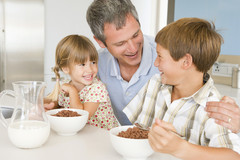 Father smiling at son and daughter eating breakfast