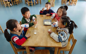 Small table of Chinese children at a table with milk and healthy snacks