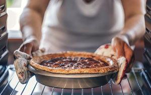 Woman removing pie from inside oven
