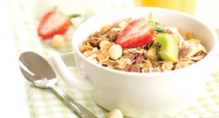 white bowl full of cereal and chopped up fruits with a spoon on the side