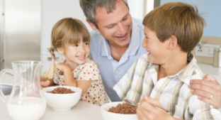 Father smiling at son and daughter eating breakfast