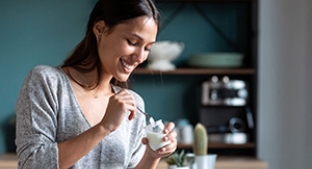 Smiling woman eating from yogurt pot