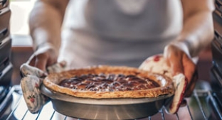 Woman removing pie from inside oven