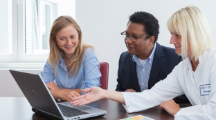 three people working at a laptop in a meeting room three people working at a laptop in a meeting room